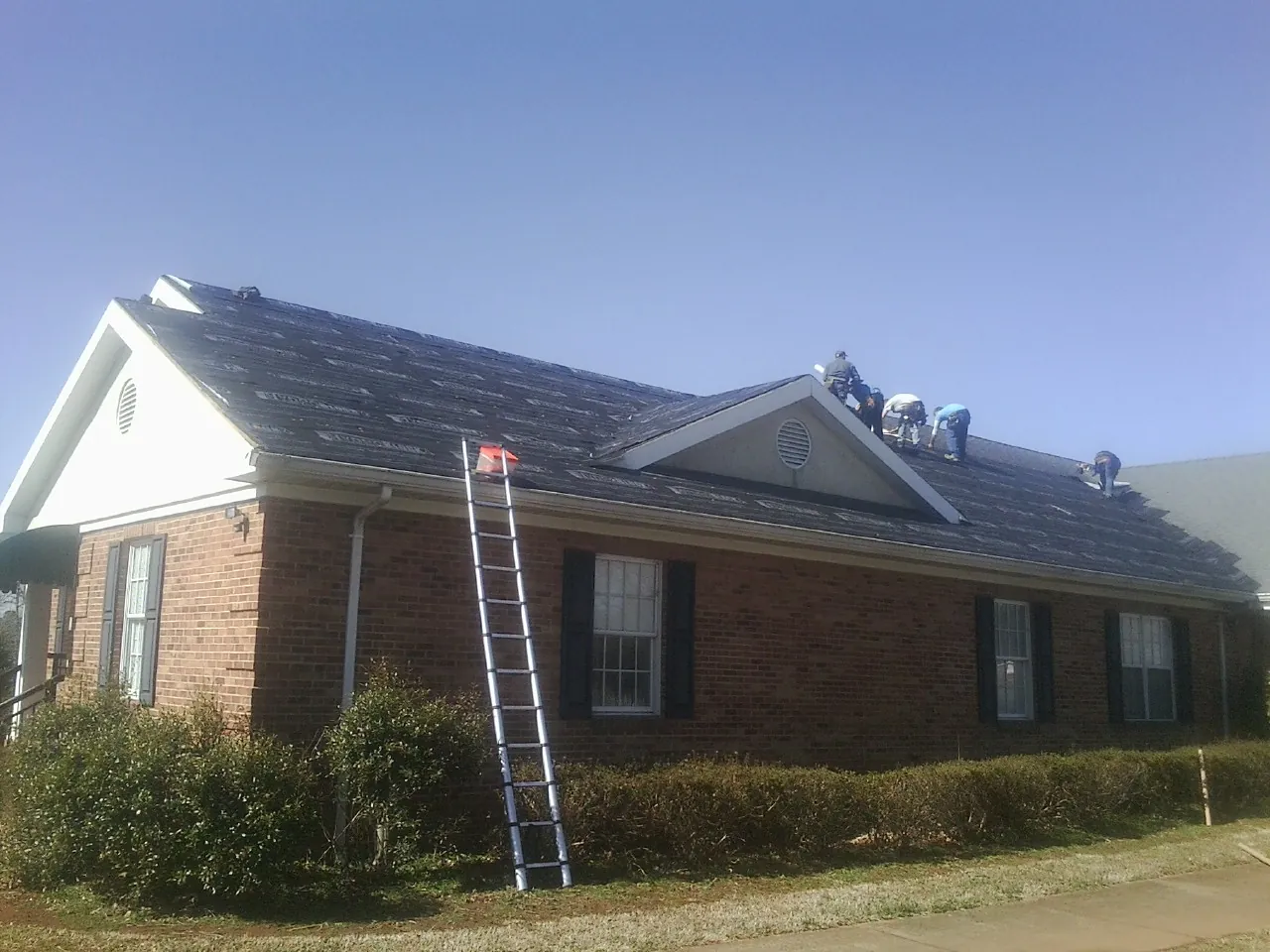 Crew tearing shingles off a brick ranch roof with a ladder set — Emergency Roof Repair work by our crew in Dearing