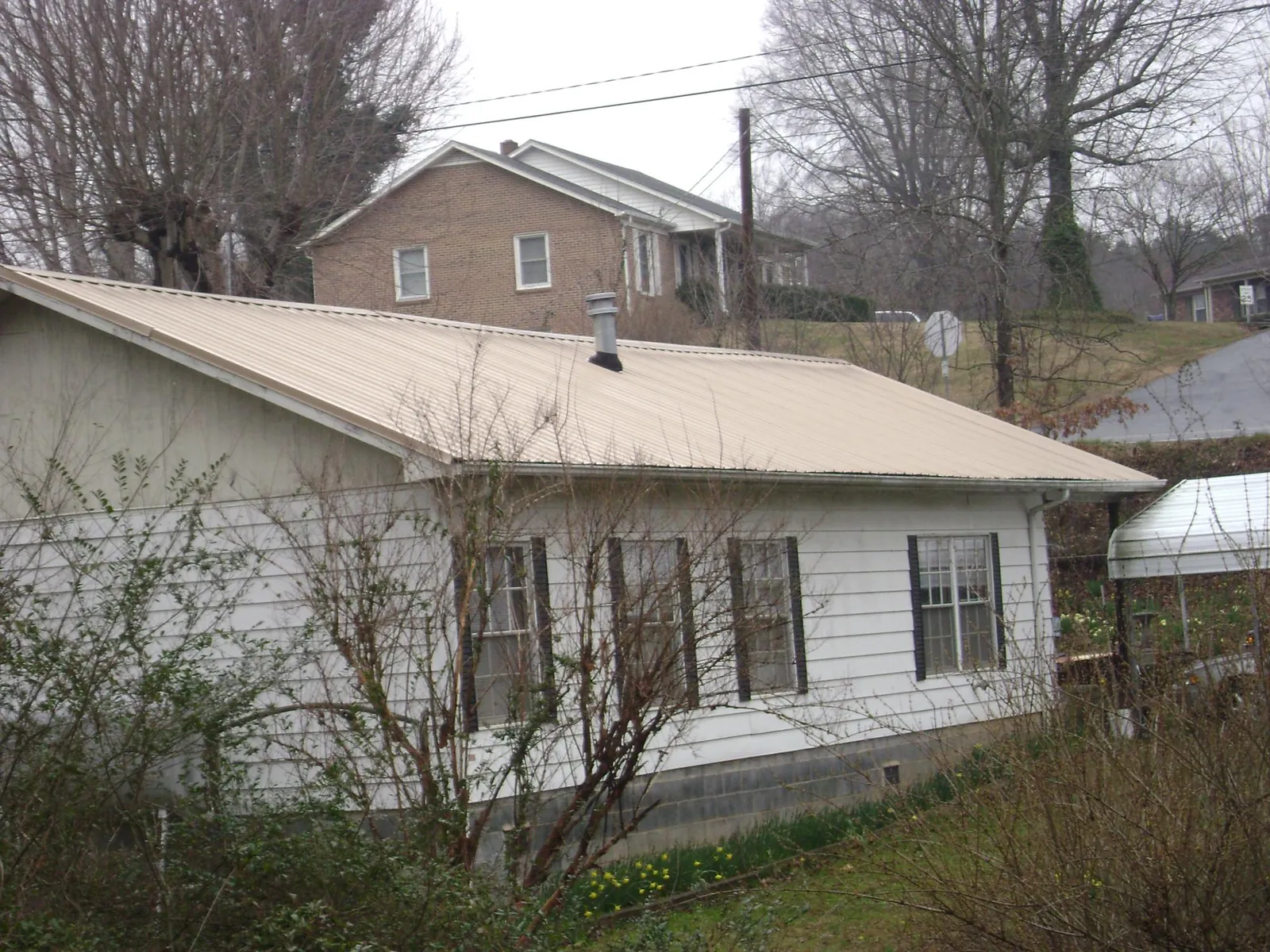 Tan metal roof on a white sided house set into a hillside — Commercial Roofing by Roofing Brothers in Dearing