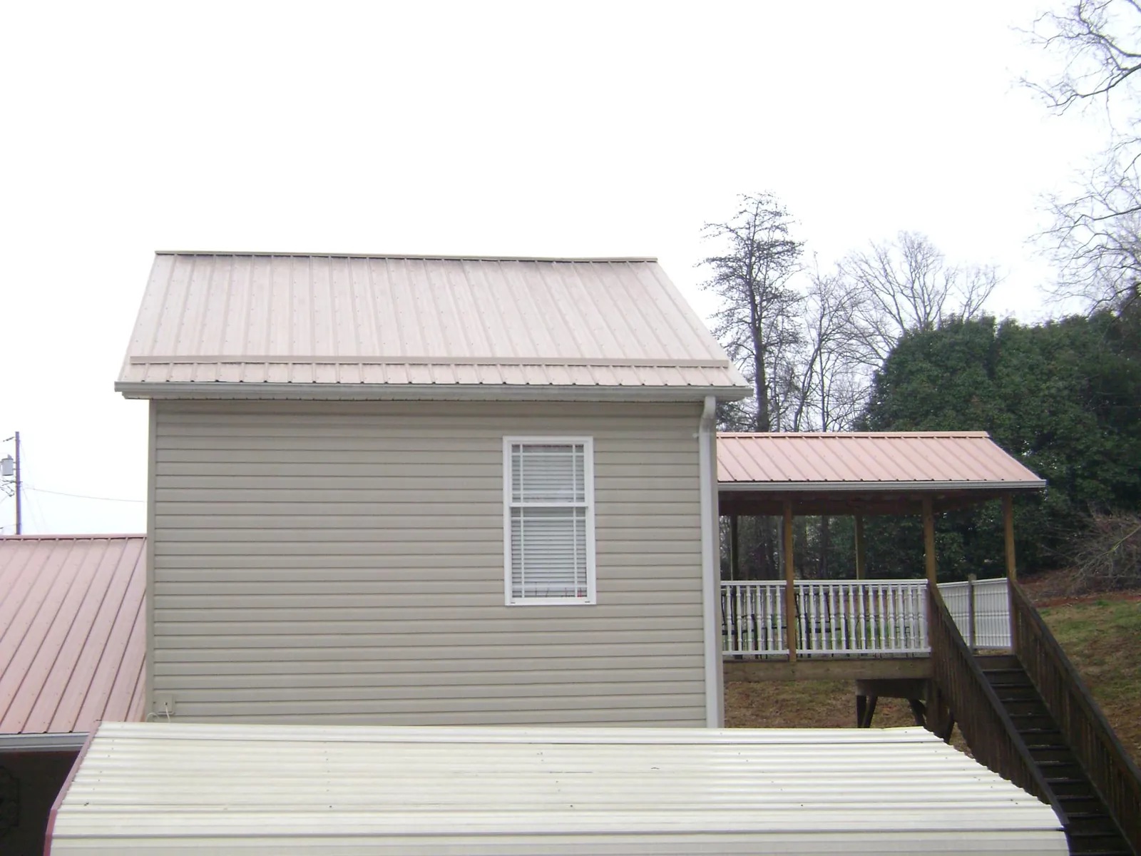 Tan metal roofs on a two story addition and attached porch, from a Roof Replacement job in Dearing